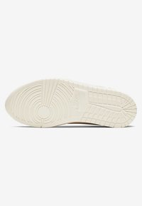 Nike-Sneakersohle in Cremefarbe, mit strukturiertem Gummi, das kreisförmige Muster und ausgeprägte Traktionsrillen aufweist. Branding sichtbar.