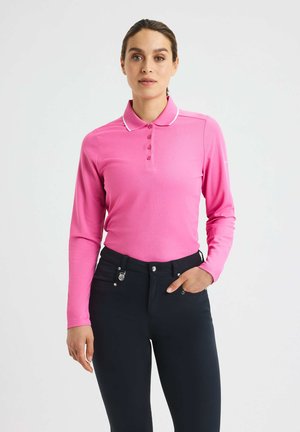 Langærmet lyserød polo t-shirt med hvid krave og knapper, parret med mørke bukser med lommer og sølvdetaljer.
