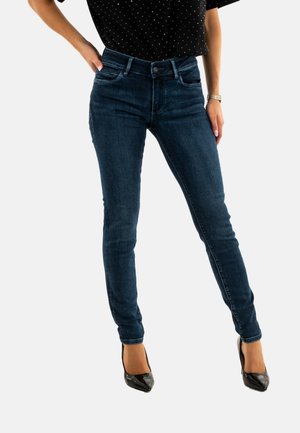 Jeans ajustados de mezclilla azul oscuro, de cintura alta y con una textura suave. Combinados con tacones altos de charol negros para un look ceñido.