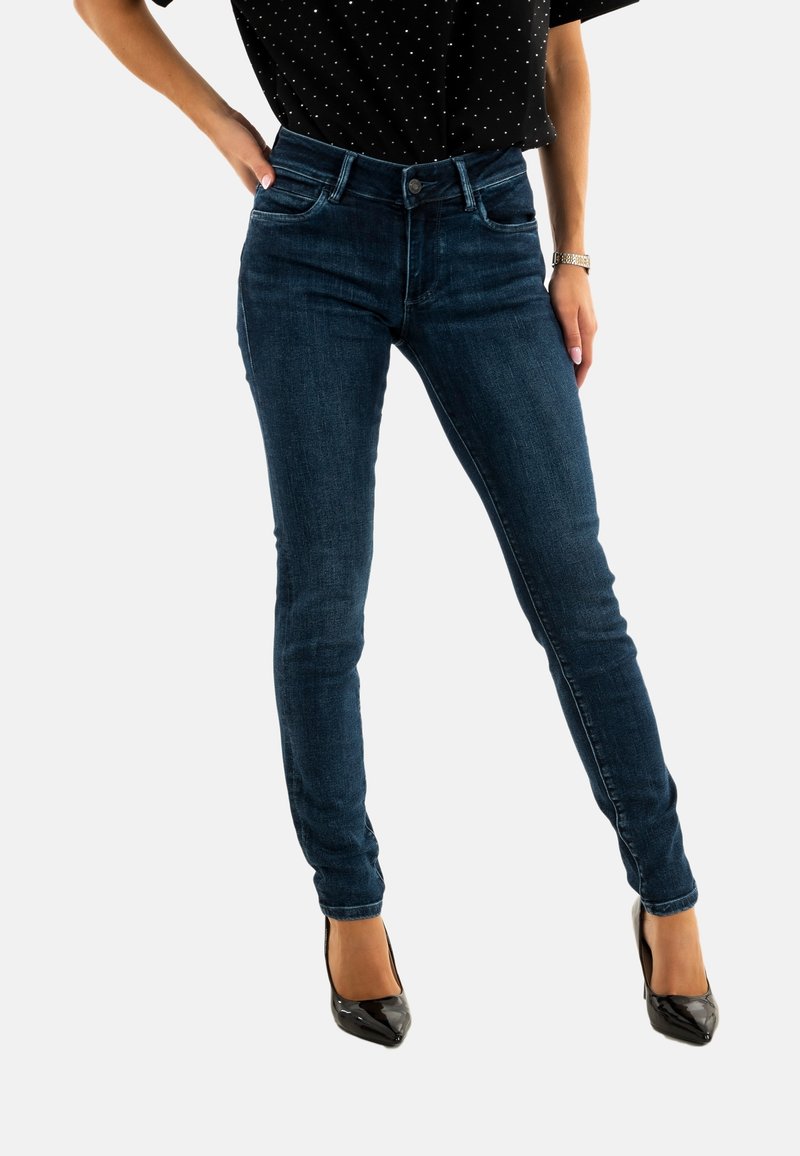 Jeans ajustados de mezclilla azul oscuro, de cintura alta y con una textura suave. Combinados con tacones altos de charol negros para un look ceñido.