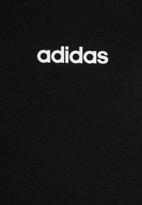 Un tessuto nero con una texture liscia presenta un logo "adidas" bianco centrato nella parte superiore. Il design è minimalista e diretto.