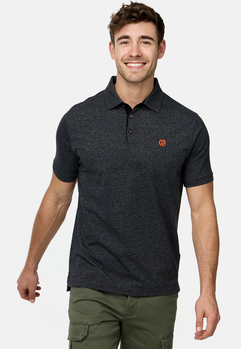 Polo shirt gris foncé à manches courtes, en tissu texturé, avec patte de boutonnage à trois boutons et logo orange discret sur la poitrine. Porté avec un pantalon cargo.
