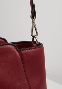 Czerwona skórzana torba o eleganckim designie, z srebrnym metalowym zapięciem i kontrastującą czarną lamówką wzdłuż krawędzi.