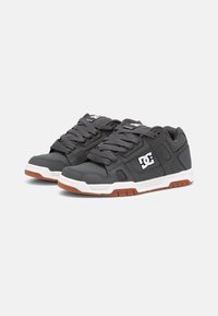 Gray sneakers with a leather upper, white accents, perforated details, and gray laces on a contrasting brown rubber sole. DC logo on the side.