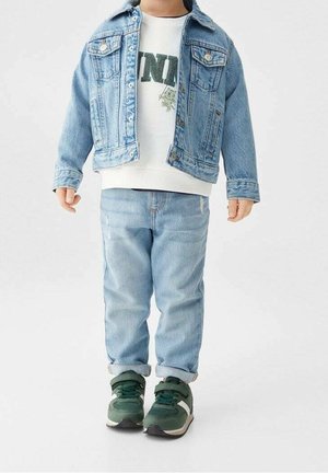 Light blue denim jacket over a white sweatshirt with green text. Light blue jeans and green sneakers with gray accents complete the outfit.