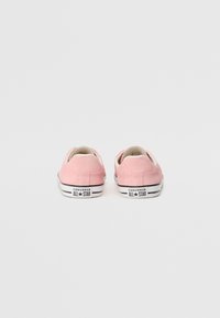 Rosa Leinenschlupfschuhe mit weicher Textur, weißem Innenfutter und schwarz-weißer gestreifter Gummisohle, die das "Converse All Star"-Logo an der Ferse trägt.
