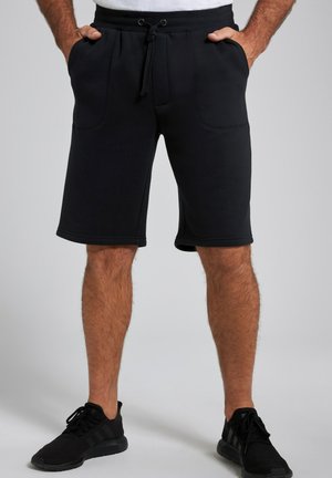 Schwarze Baumwollshorts mit einem Kordelzugbund, seitlichen Taschen und geradem Schnitt. Kombiniert mit schwarzen Sportschuhen für einen lässigen Look.