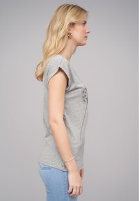 T-shirt en coton gris à manches courtes roulées, avec un imprimé de pissenlit sur le devant et un ourlet arrondi. Porté avec un jean slim bleu.