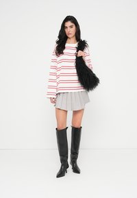 Μπλούζα με μακριά μανίκια κόκκινες και λευκές ρίγες, γκρι πλισέ μίνι φούστα, μαύρα ψηλοτάκουνα μπότες μέχρι το γόνατο και μια μαύρη τσάντα με υφή.