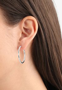 Pendiente de aro plateado colgando de una oreja, con una textura suave y brillante y un diseño circular, con un perfil delgado y minimalista.
