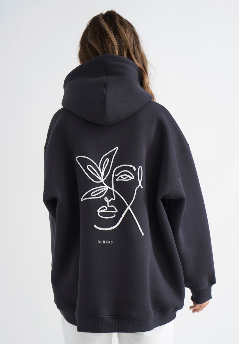 Felpa nera oversized con una linea bianca che disegna un volto e un design floreale sul retro; presenta un cappuccio con stringhe e polsini a coste.