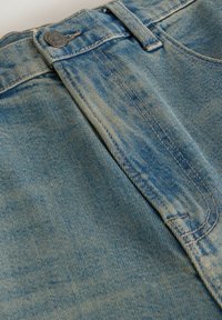 Gros plan sur un jean en denim bleu clair montrant les détails du bouton, des passants de ceinture et de la couture de la poche avant.