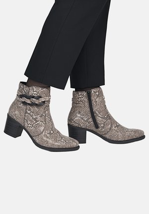 Ankle boots with snakeskin pattern and block heels worn with black pants, featuring a side zipper and braided strap detail.