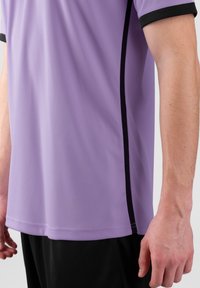 Paarse sportshirt met zwarte rand en zijstrepen, met een gladde stofstructuur en korte mouwen. Aangekleed op heuplengte.