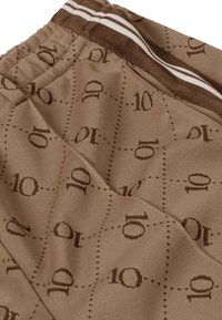 Brązowe sportowe spodenki z teksturą wzoru z powtarzającymi się motywami „10”, wykonane z miękkiej tkaniny, z elastycznym pasem w białe paski.