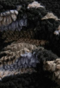 Teksturowana tkanina z mieszanką czarnych, beżowych i stonowanych niebieskich włókien, tworząca miękką, pluszową powierzchnię z falistym wzorem.