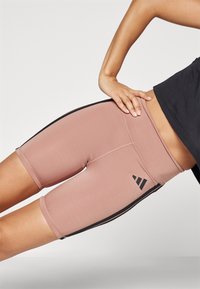 Shorts de vélo ajustés en rose, fabriqués en tissu extensible. Présentent des rayures noires sur les côtés et un accent de logo triangulaire sur la cuisse.