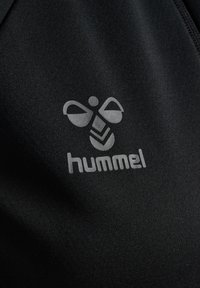 Schwarzer Stoff mit glatter Textur, auf dem ein graues Logo einer stilisierten Biene und der Markenname "hummel" darunter zu sehen sind.