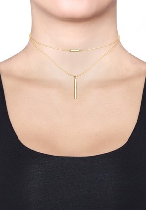 Gouden gelaagde choker ketting met twee kettingen. De bovenste ketting heeft een horizontale staaf, en de onderste ketting heeft een verticale hanger.
