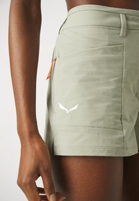 Ljusgröna sportshorts med en slät yta, med en orange dragsko, sidoficka och en vit logodetalj.