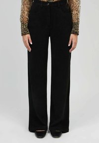 Pantalons noirs à jambes larges en tissu doux, dotés d'une fermeture à bouton, de poches avant et d'une texture lisse. Associés à un haut à motif léopard.
