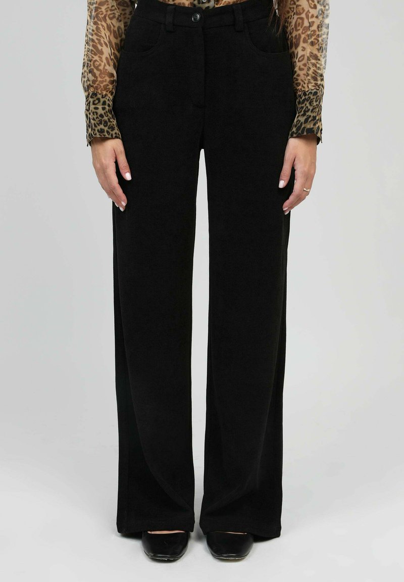 Pantalons noirs à jambes larges en tissu doux, dotés d'une fermeture à bouton, de poches avant et d'une texture lisse. Associés à un haut à motif léopard.
