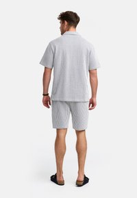 Camisa de manga corta a rayas y pantalones cortos a juego en gris claro y blanco. La tela es ligera. Presenta un collar informal y un ajuste relajado.