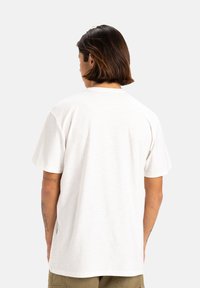 T-shirt bianco a maniche corte con colletto rotondo, tessuto morbido e vestibilità comoda. Tatuaggi visibili sul braccio, senza ulteriori dettagli.