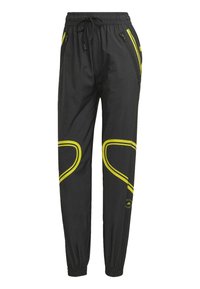 Černé sportovní kalhoty s elastickými manžetami, páskem na zavazování, zipovými bočními kapsami a žlutými zakřivenými pruhy kolem kolen a kapes.