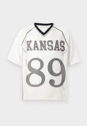 Λευκό αθλητικό φανελάκι από δίχτυ με μαύρο περίγραμμα, με την επιγραφή "KANSAS" στο στήθος και μεγάλο αριθμό "89" από κάτω.
