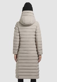 Cappotto puffo beige chiaro con cuciture orizzontali, cappuccio rimovibile e maniche lunghe. Presenta un orlo regolabile e tasche laterali.