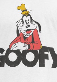 Valkoinen puuvillainen t-paita, jossa on painettu grafiikka sarjakuvakoirasta, jolla on mustavalkoiset piirteet, punainen paita ja keltainen hattu. Teksti lukee "GOOFY".