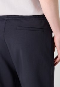 Marina blå byxor med en slät yta och enkel design, med en enda bakficka utan synlig hårdvara eller mönster.