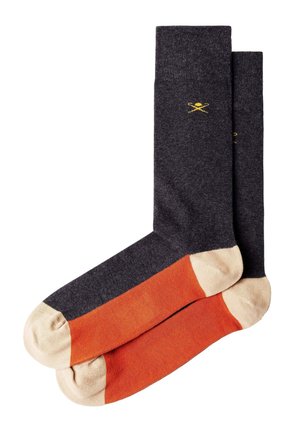Calcetines gris oscuro con parte media naranja y dedos y talones beige, con un pequeño logo amarillo de cucharas cruzadas cerca de la parte superior.
