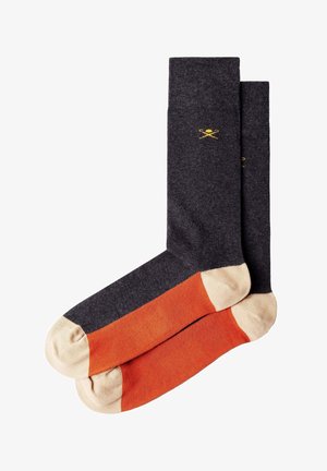Calcetines gris oscuro con parte media naranja y dedos y talones beige, con un pequeño logo amarillo de cucharas cruzadas cerca de la parte superior.