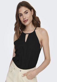 Top negro sin mangas con un corte en forma de ojo de llave, tejido ligero y tirantes delgados, combinado con pantalones de cintura alta en color crema.
