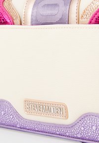 Sac en tissu beige texturé avec des accents violets, détail de logo métallique et un mélange d'éléments scintillants roses et dorés.
