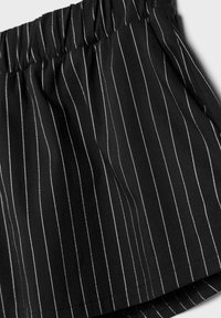 Čierne pruhované šortky s elastickým pásom, vyrobené z hladkej tkaniny. Majú tenké vertikálne biele pruhy a uvoľnený strih.