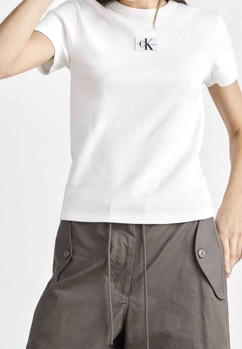 Bílý pruhovaný bavlněný tričko s malým obdélníkovým logem CK na hrudi, spárované s olivově zelenými cargo šortkami s knoflíkovými kapsami.
