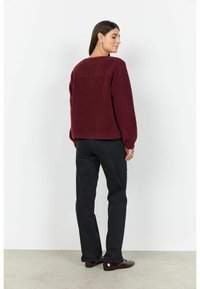 Burgundy fleece jacket with a textured surface, boxy shape, dropped shoulders, and a square back yoke, paired with black straight-leg pants.