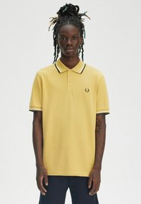 Polo giallo a maniche corte, con un collo a righe nere e bianche in contrasto e una pattina con tre bottoni. Logo Freestyle sul petto.