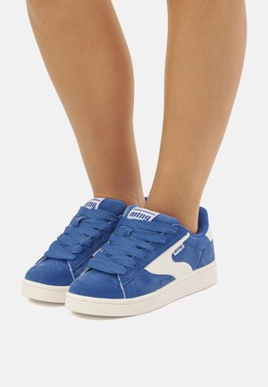 Sneaker in suede blu con accenti bianchi, caratterizzati da punta rotonda, suola in gomma spessa e design dei lacci testurizzato. Logo visibile sulla linguetta.