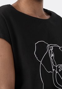 Svart T-shirt med korta ärmar, med en vit linjeteckning av en elefant på framsidan. Mjuk bomullsmaterial, avslappnad halsringning.