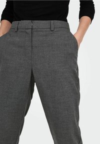 Pantaloni grigi in tessuto testurizzato, con frontale piatto, tasche laterali e una leggera lucentezza. Presentano passanti per cintura e un design snello.