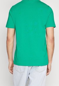 Camiseta de algodón verde con mangas cortas y cuello redondo; textura lisa; el dobladillo termina por encima de la cintura, combinada con pantalones vaqueros claros.