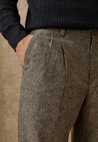 Trousers in textured grey fabric with a herringbone pattern, featuring side pockets and a tailored fit, paired with a knit black sweater.