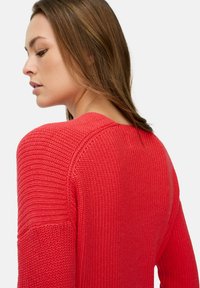 Roter Strickpullover mit strukturierter Rippstruktur, weitem Halsausschnitt und überschnittenen Schultern, aus einem schrägen Blickwinkel von hinten präsentiert.