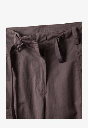 Braune Hose mit teilweise geöffnetem Reißverschluss, Stoffgürtel, der durch die Schlaufen geführt ist, und Kunststoffschnalle am Bund.