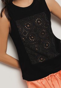 Top nero senza maniche con un pannello in pizzo testurizzato e fori circolari; corpo in tessuto liscio; abbinato a pantaloni arancioni larghi con coulisse.