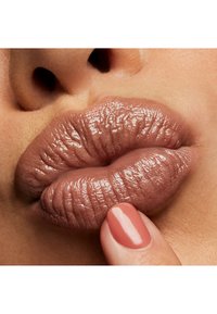 Gros plan sur des lèvres pleines d'une teinte nude-brune brillante et d'une texture fine ; une main avec un vernis corail accentue le look.